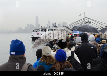 New York, NY, USA, le 26 novembre 2013. Les touristes visitant la Statue de la liberté attendre le bateau Statue Cruises dans une averse. Une tempête hivernale qui remonte la côte Est des États-Unis menace plans de voyage pour l'action de grâce. Crédit : Jennifer Booher/Alamy Live News Banque D'Images