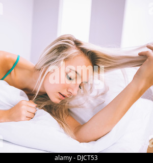 Calme superbe blonde lying on bed holding her hair Banque D'Images