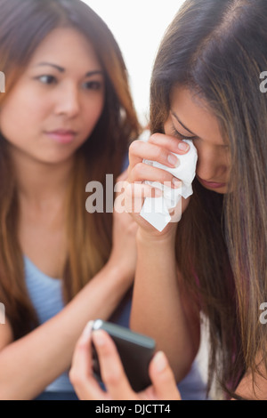 Femme malheureuse à la recherche de téléphone à être réconforté par sa sœur Banque D'Images