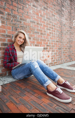 Happy gorgeous student leaning against wall using laptop Banque D'Images