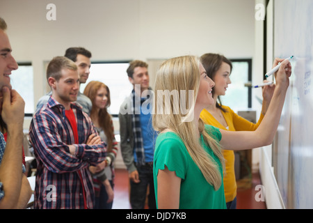 Les élèves écrire sur le tableau blanc ensemble en classe pendant que d'autres regardent Banque D'Images