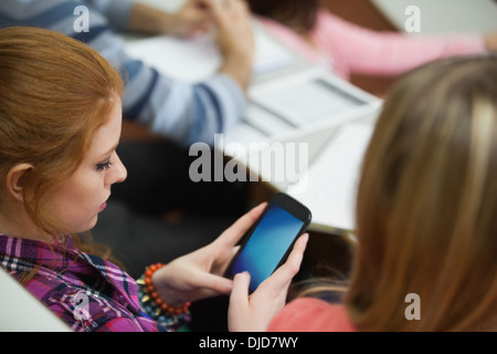 Student sitting in a lecture hall des SMS sur son smartphone Banque D'Images