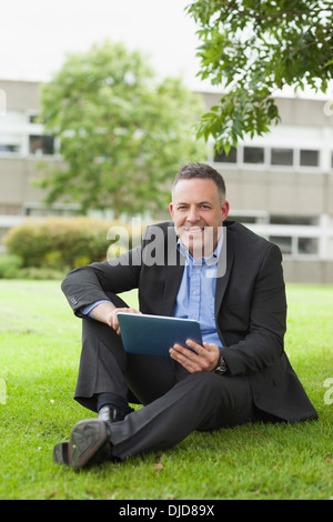 Maître gai en utilisant sa tablette pc assis dehors sur le campus Banque D'Images