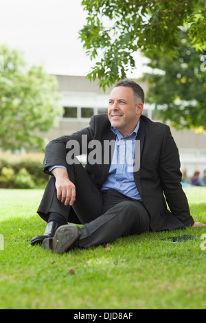 Professeur souriant assis dehors sur le campus à la suite Banque D'Images
