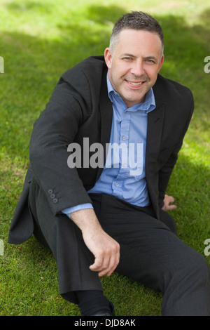 Professeur souriant assis dehors sur le campus à la recherche jusqu'à l'appareil photo Banque D'Images