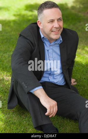 Professeur souriant assis dehors sur le campus jusqu'à pensivement Banque D'Images