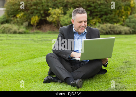 Professeur souriant assis dehors sur le campus en utilisant son ordinateur portable Banque D'Images