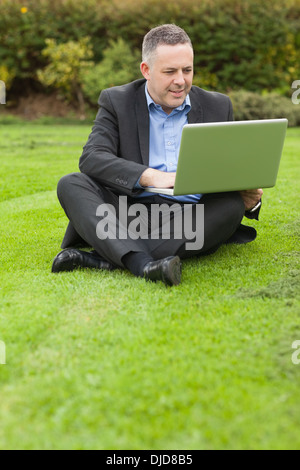 Conférencier heureux assis dehors sur le campus en utilisant son ordinateur portable Banque D'Images