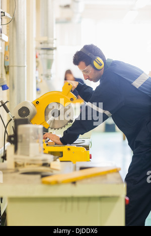 Artisan avec des lunettes de scier un morceau de bois Banque D'Images