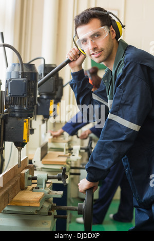 Smiling artisan avec des lunettes de perçage d'un morceau de bois Banque D'Images