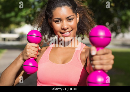 Smiling fit young woman exercising with dumbbells in park Banque D'Images