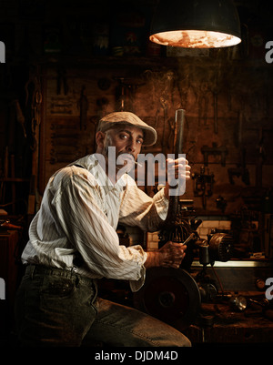 Homme avec chapeau et allume la réparation d'un moteur dans un atelier Banque D'Images
