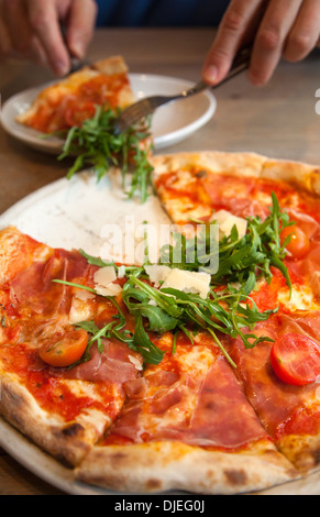 La prise de l'homme tranche de San Daniele Pizza avec rucola et prosciutto Banque D'Images