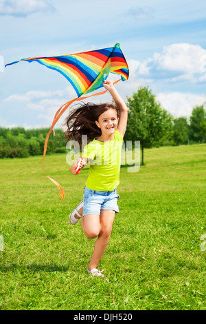 Happy little girl avec kite courir dans le parc avec cerf-volant avec sourire et renoncer à de longs poils sur le vent Banque D'Images