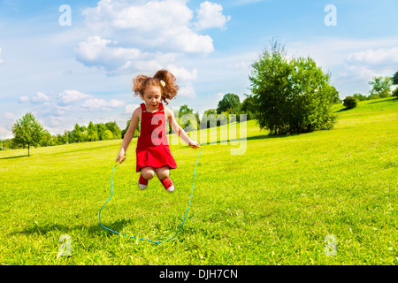 Belle petite fille de 6 ans saute au-dessus de la corde dans le parc aux beaux jours d'été Banque D'Images