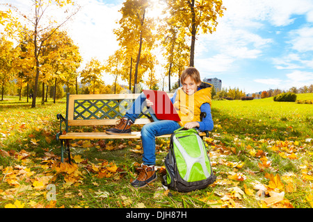 Portrait of happy 10 ans garçon assis sur le banc avec sac à dos sac à dos avec document lecture après l'école Banque D'Images