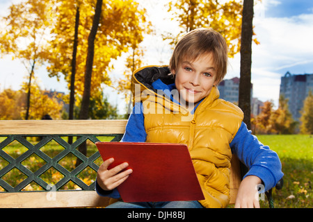 Fermer portrait of happy 10 ans garçon assis sur le banc avec sac à dos sac à dos avec document lecture après l'école Banque D'Images