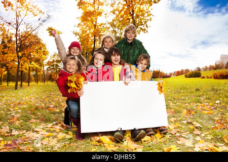 Happy smiling groupe d'enfants, d'amis, garçons et filles, montrant l'étiquette vierge de sélection de l'écrire sur votre propre texte à l'automne parc avec arbres d'érable Banque D'Images