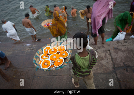Un garçon vend aux gens qui font des ablutions dans le Gange, petites bougies avec des fleurs pour l'utiliser comme offrandes. Banque D'Images
