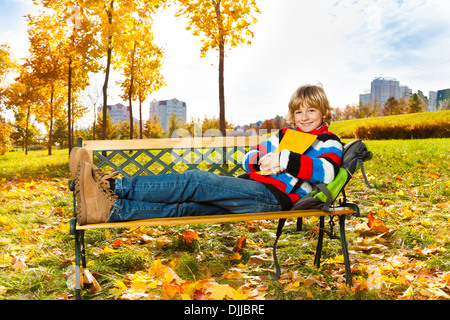 Joli garçon blond assis sur le banc avec livre smiling et heureux Banque D'Images