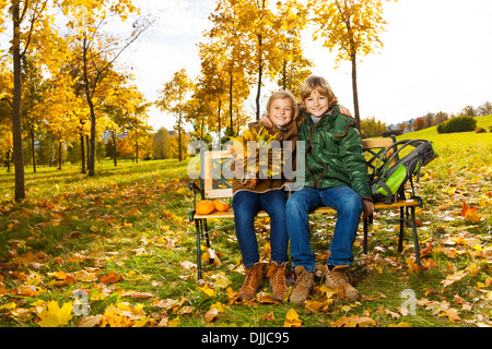 Portrait de deux enfants blonds heureux assis sur le banc du parc en automne Banque D'Images