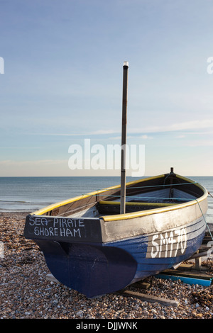 Petit bateau de pêche repose sur une plage de galets dans le soleil de l'après-midi. Banque D'Images