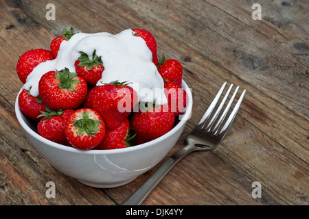 Les Fraises et la crème dans un bol contre un arrière-plan de table rustique Banque D'Images