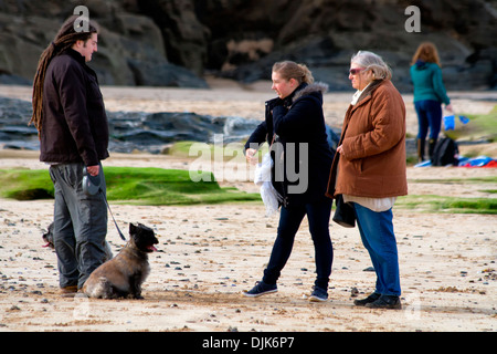 Jeune homme avec des dreadlocks, promenait son chien, rencontre deux femmes sur une plage de Cornouailles, Angleterre Banque D'Images