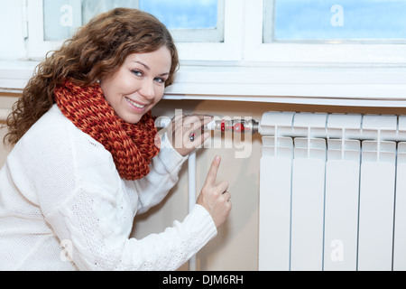 Happy woman gesturing lorsque controling thermostat sur radiateur de chauffage central Banque D'Images