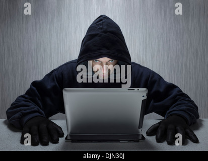 Un homme à capuchon représentant un criminel cybernétique, à la recherche d'un ordinateur tablette. Banque D'Images
