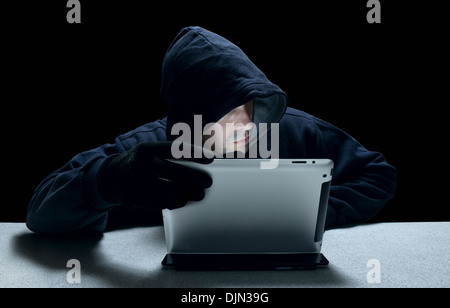 Un homme à capuchon anonyme représentant un criminel cyber, à l'aide d'un ordinateur tablette. Banque D'Images