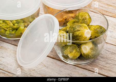 Les restes de repas ou dîner (poulet, choux de Bruxelles, asperges, petits pois) stockés dans des récipients en verre Banque D'Images