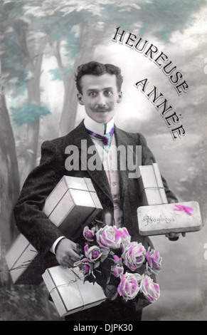 Carte postale de voeux vintage d'un jeune homme français avec des cadeaux et des fleurs pour le Nouvel An, vers 1910. Banque D'Images