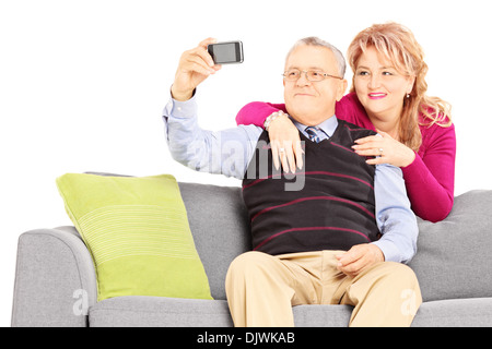 Heureux l'homme d'âge moyen et la femme assise sur un canapé moderne à prendre des photos d'eux-mêmes avec un téléphone mobile Banque D'Images
