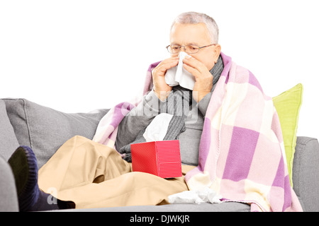 L'homme principal couvert de couverture sur un canapé soufflant son nez dans un mouchoir Banque D'Images