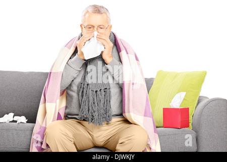Sick man covered with blanket assis sur un canapé et en soufflant son nez Banque D'Images