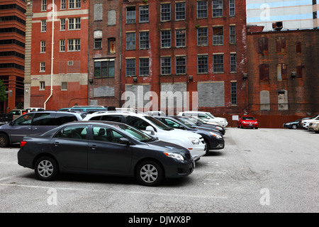 Nouvelles voitures dans un parking devant de vieux bâtiments industriels abandonnés en briques dans le centre de Baltimore, Maryland, États-Unis Banque D'Images