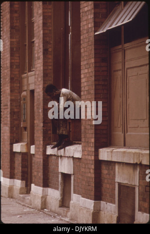 Une photo d'un homme noir assis sur le rebord d'une fenêtre d'un bâtiment dans une zone à forte criminalité sur le South Side de Chicago. L’image capture un moment reflétant la pauvreté urbaine et le chômage au XXe siècle. Banque D'Images
