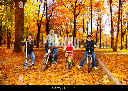 Groupe de garçons noirs et les petites filles, frères et soeur la bicyclette et scooter dans l'automne Octobre park avec feuilles d'érable Banque D'Images