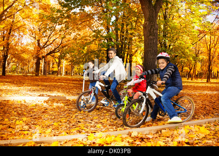 Groupe de quatre garçons noirs et les petites filles, frères et soeur la bicyclette et scooter dans l'automne Octobre park avec feuilles d'érable Banque D'Images