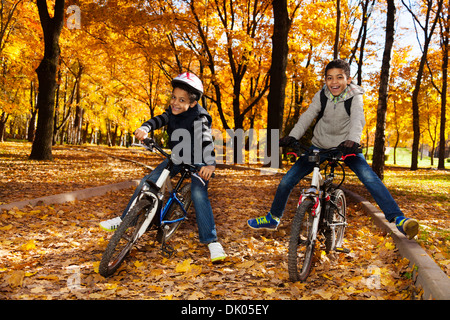 Deux noirs 8 et 10 ans garçons monter un vélo à l'automne et de l'érable Oak tree Park Banque D'Images