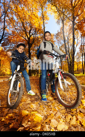 Deux cute black smiling 8 et 10 ans les garçons de la bicyclette, le port de casque à l'automne et de l'érable Oak tree Park Banque D'Images