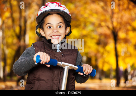 Fermer portrait of happy smiling 5 ans black boy wearing helmet riding scooter en automne Banque D'Images