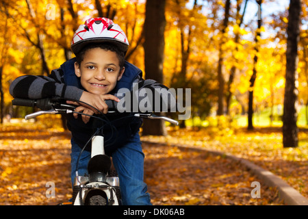 Fermer portrait of happy smiling 8 ans garçon noir rouler à vélo dans le parc automne leaning on location stern Banque D'Images