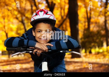 Fermer portrait of happy smiling 8 ans garçon noir rouler à vélo dans le parc de l'automne s'appuyant sur l'arrière port casque de vélo Banque D'Images