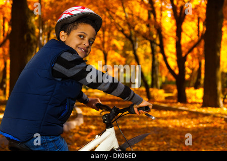 Fermer portrait of happy smiling 8 ans garçon noir rouler à vélo dans le parc automne leaning on location stern se retourner Banque D'Images