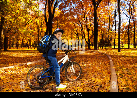Happy smiling 8 ans garçon noir sac à dos avec le vélo dans le parc automne leaning on location stern se retourner Banque D'Images