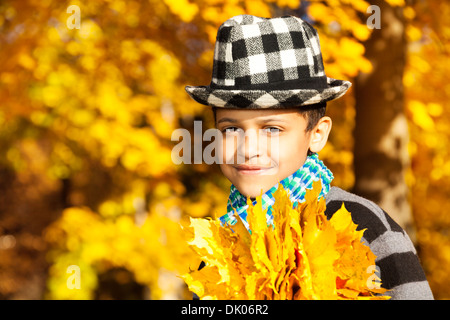 Fermer portrait of happy 8 ans boy wearing hat and holding bouquet de feuilles d'oranger à l'érable Banque D'Images