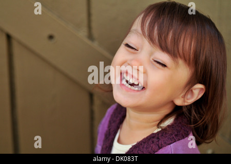 Un enfant de deux ans M. mixed race female rit tout en ayant sa photo prise. Elle a les cheveux bruns et porte une chemise violette. Banque D'Images