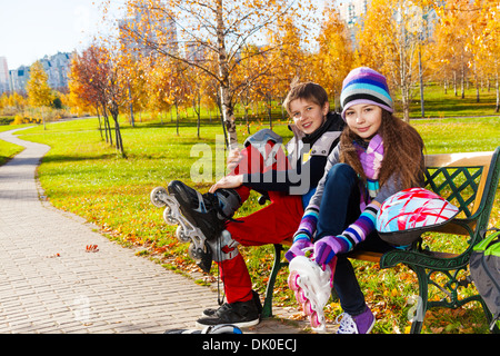 Mettre sur rollers Enfants 10 et 11 ans couple d'enfants de l'école, un garçon fille en vêtements automne chaud sur le banc dans le parc Banque D'Images